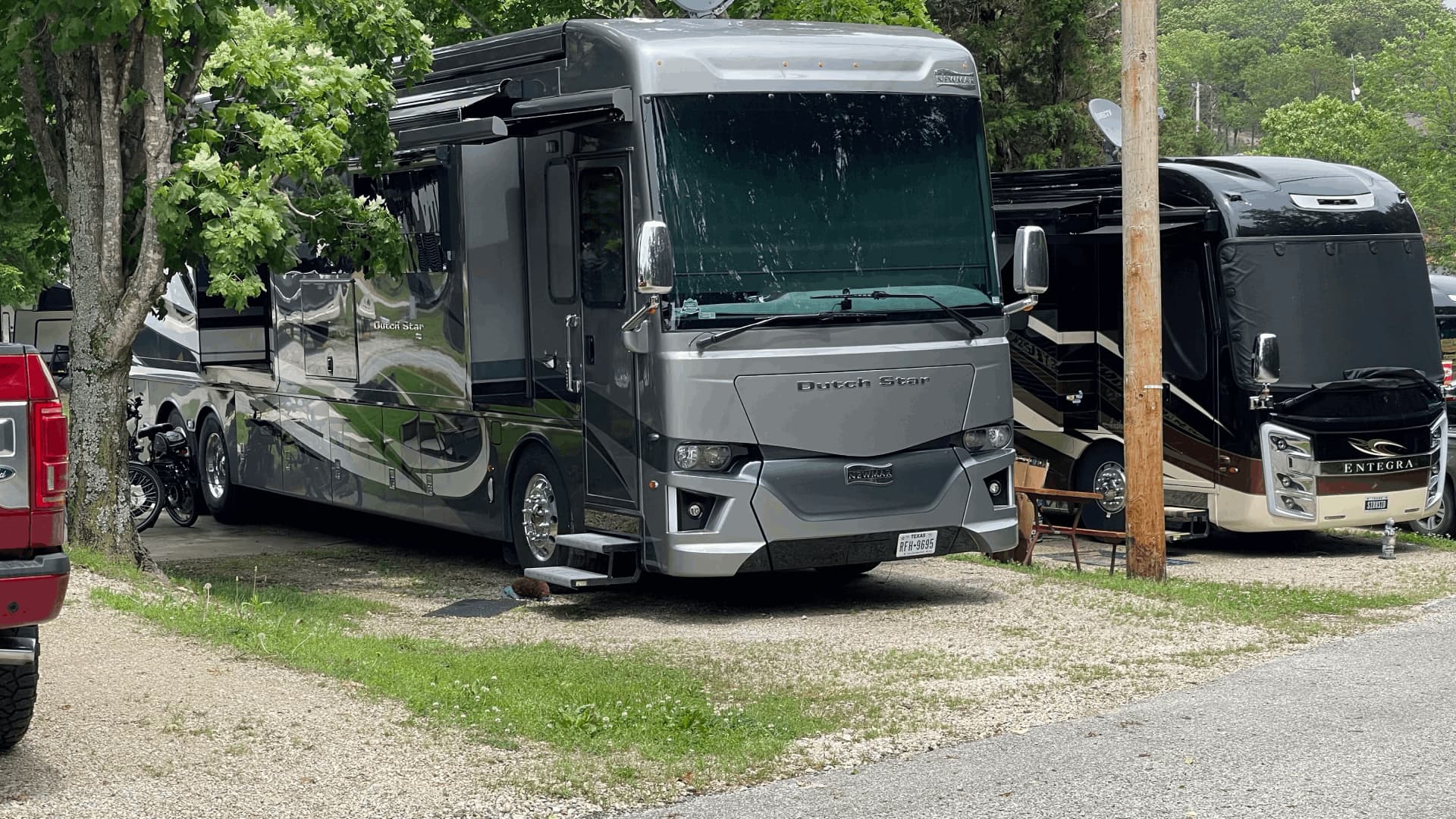 A silver and black RV is parked in a gravel lot